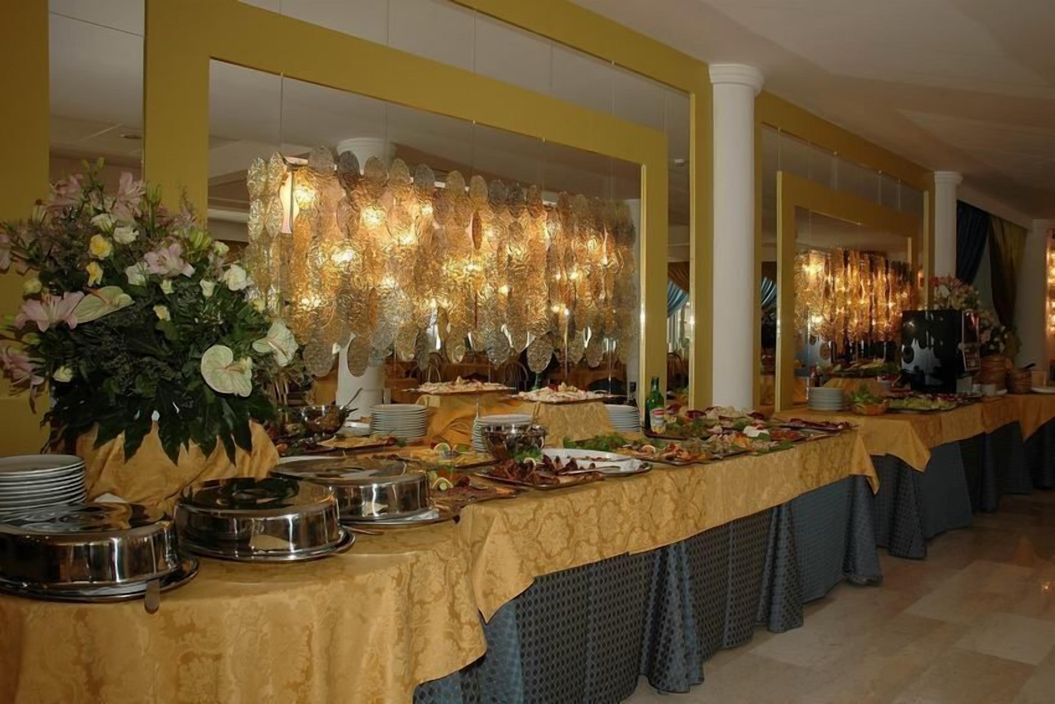 Ein reichhaltiges Buffet mit mehreren Servierstationen, einem floralen Mittelstück und einer Wand mit hängenden Lampen.