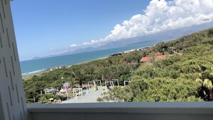 Uitzicht vanuit een raam op een kustgebied met strand, groen en een heldere lucht.