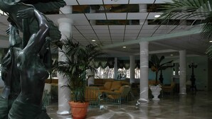 Een ruime lobby met een groot standbeeld, potplanten en een zithoek met gele stoelen.