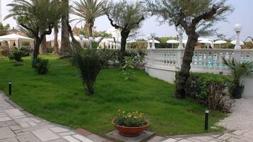 A well-maintained garden with palm trees, a swimming pool, and a white fence.
