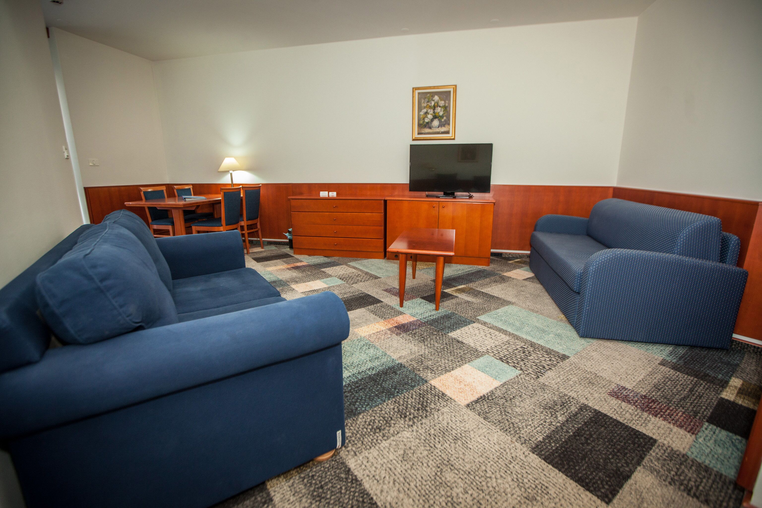 Una sala de estar con un sofá azul, un sillón a juego, un mueble de madera, un televisor y un comedor con mesa y sillas.
