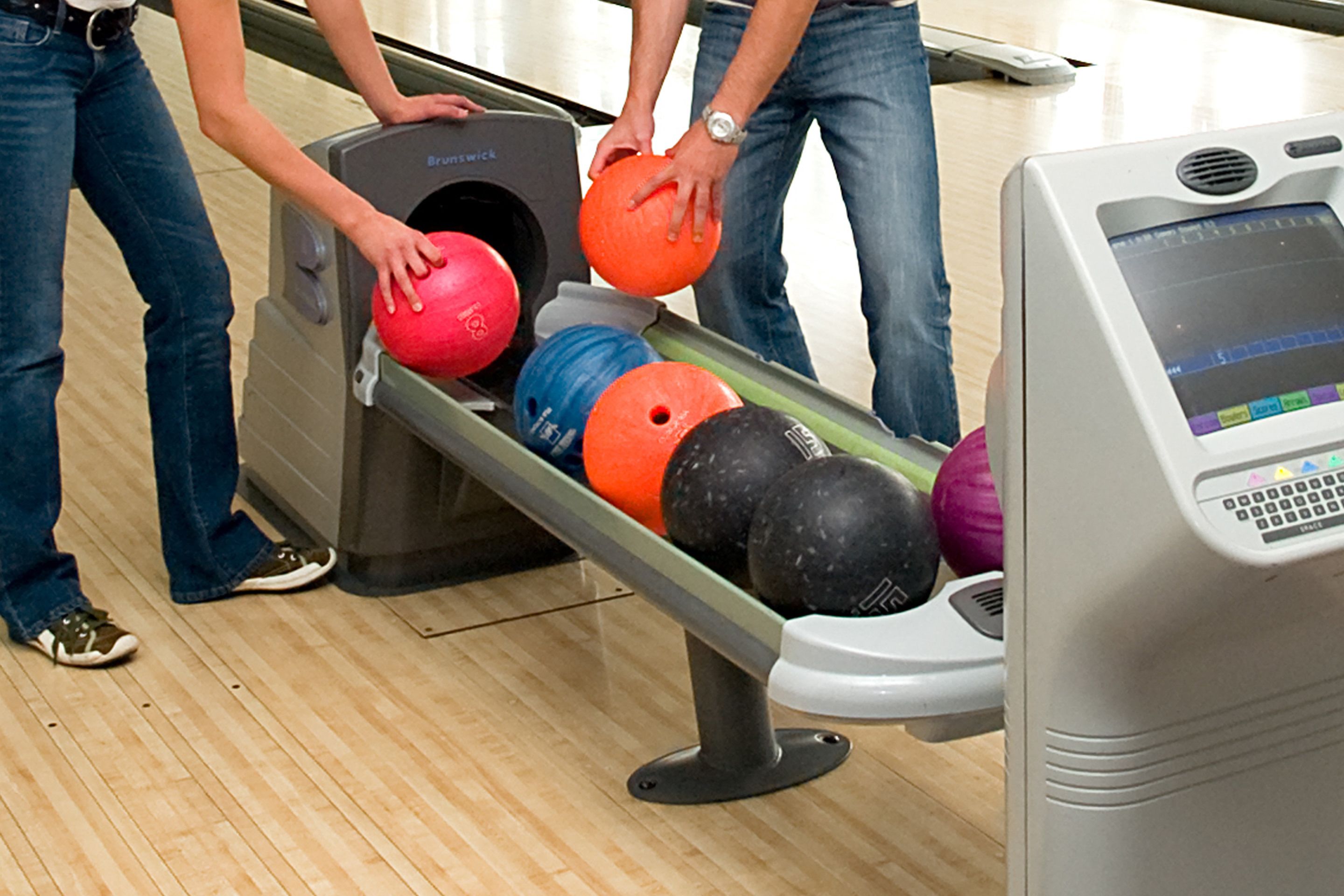 A bowling lane with multiple bowling balls and a bowling machine.