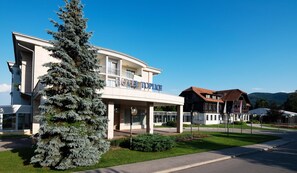A hotel with a modern facade, a prominent entrance, and a large tree in the foreground. - Hotel Toplice (Brezice)