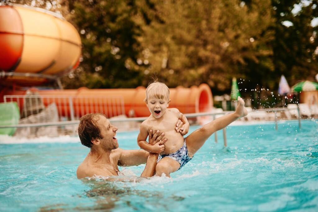 A person in a swimming pool with a child being lifted.