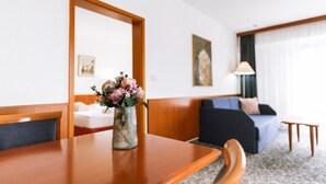 Una habitación de hotel con una mesa de madera, un florero con flores, una cama, un sofá de color oscuro y un cuadro en la pared.