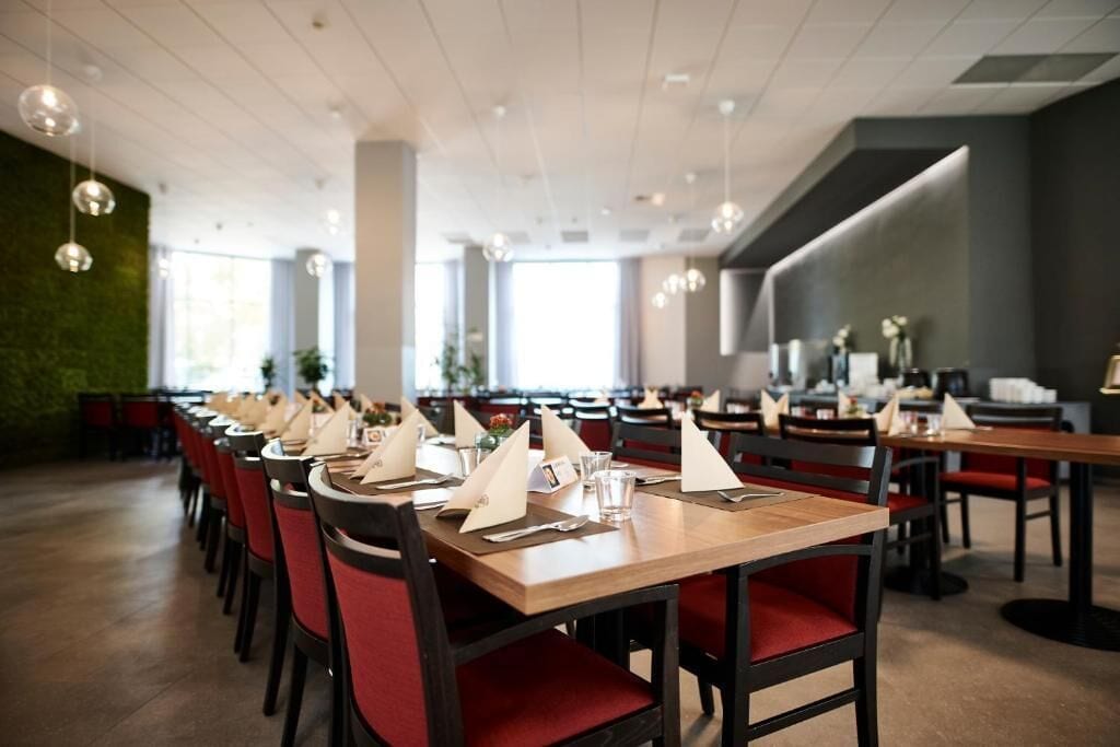 Un restaurante con varias mesas preparadas para comer, con sillas rojas y mesas de madera.