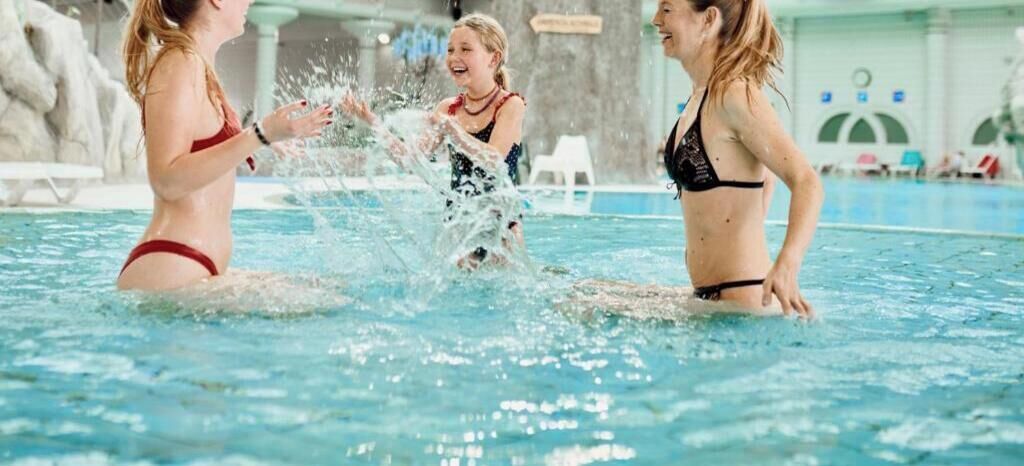 En indendørs swimmingpool med tre personer i vandet.
