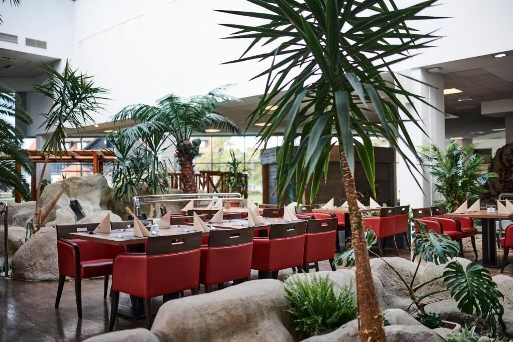 An indoor dining area with tables and chairs, surrounded by tropical plants and rocks.