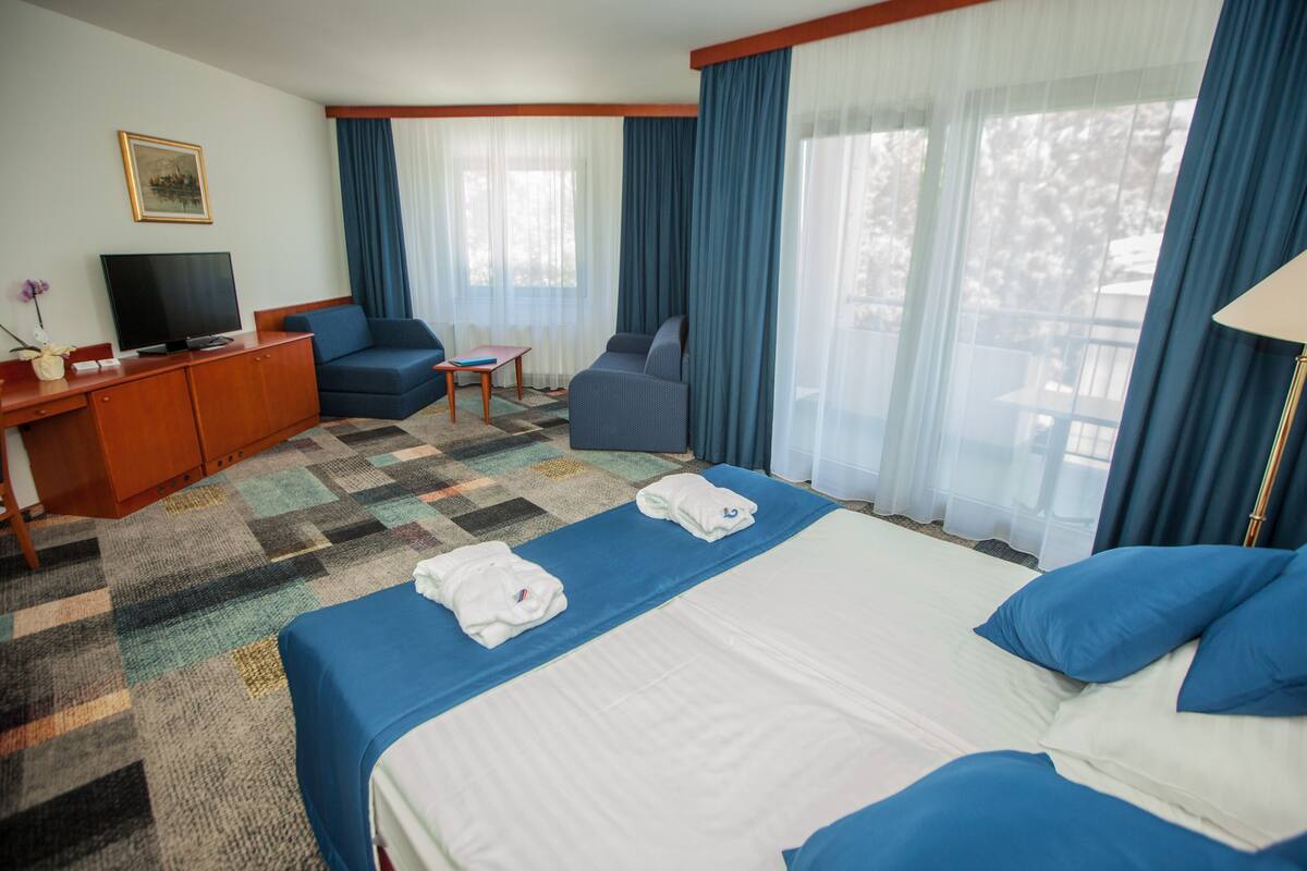 A hotel room with a large bed, two armchairs, a TV, and a desk.