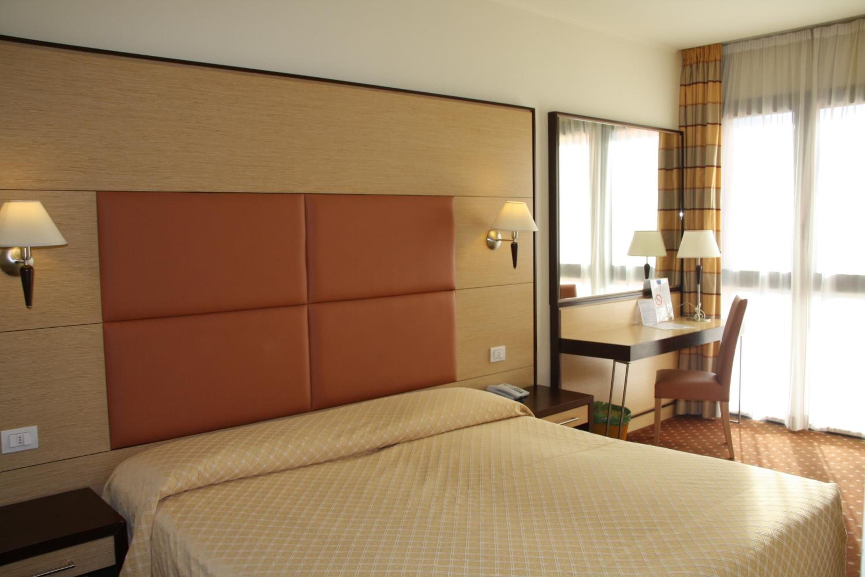 Une chambre d’hôtel avec un grand lit, un bureau, une chaise et un miroir.