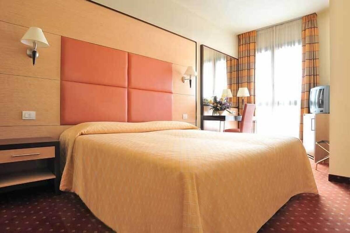 A hotel room with a large bed, a desk with a chair, a television, and a window with curtains.