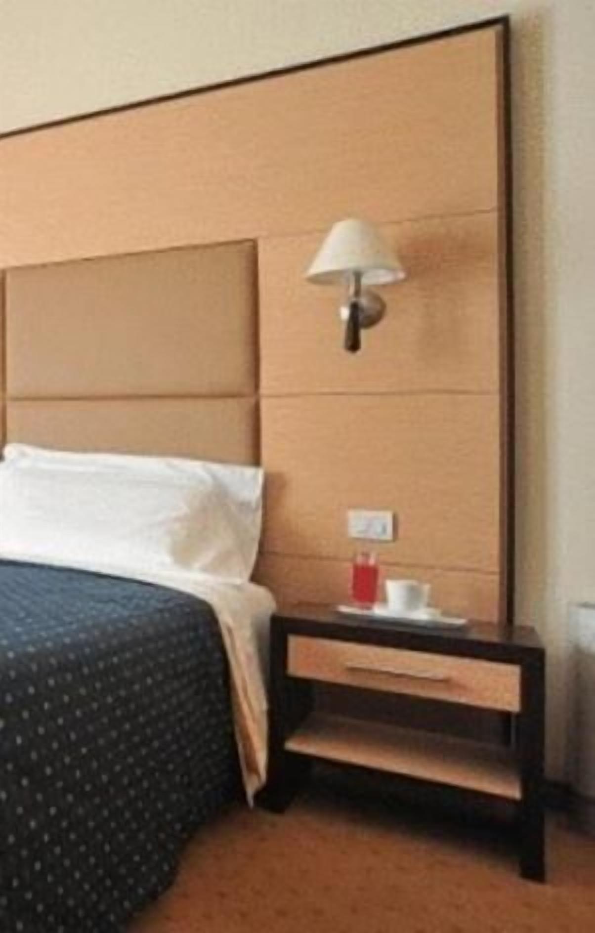 A hotel room with a large bed, a nightstand with a lamp, and a small table with a cup.