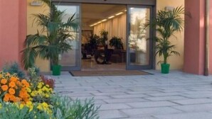 A building entrance with a glass door, potted plants, and a tiled patio area. - Inn Hotel (Barberino di Mugello)