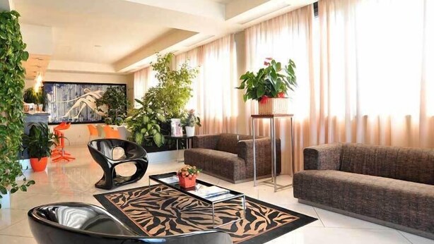 A modern living room with a sofa, a coffee table, and a chair. There are several potted plants and a painting on the wall. - Inn Hotel (Barberino di Mugello)