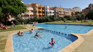 A swimming pool surrounded by multi-story buildings with balconies, a grassy area, and people enjoying the pool. - Apartaments Comte d'Empuries (Castello d'Empuries)