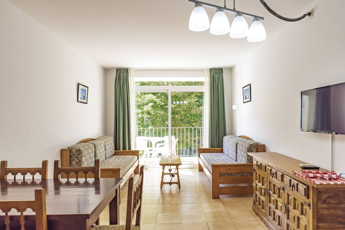A room with a dining table, two sofas, a wooden cabinet, and a TV.