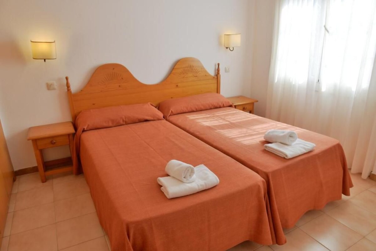A double room with two beds, each with a wooden headboard, and a nightstand between them. There are two wall-mounted lamps on either side of the bed.