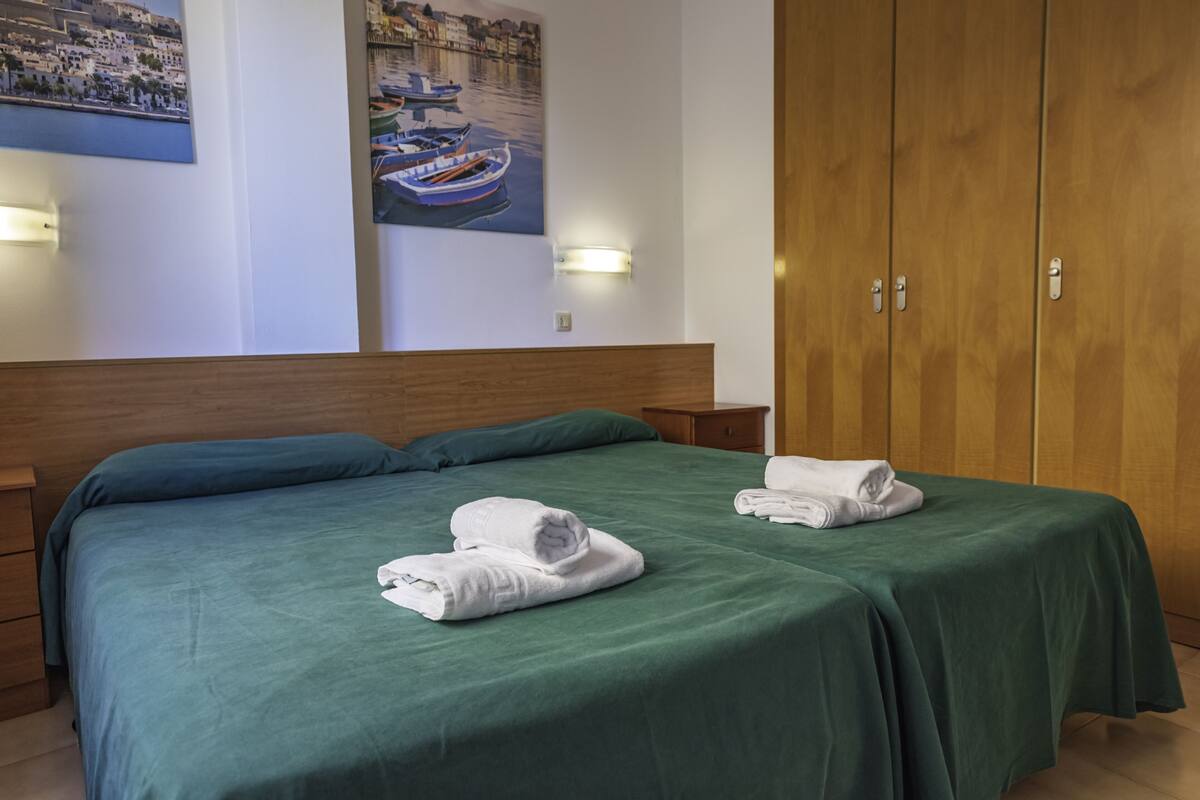 A hotel room with a bed, two nightstands, a wooden wardrobe, and two wall-mounted light fixtures.