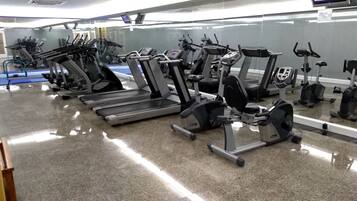 Un gimnasio con diversos equipos de ejercicio, incluyendo cintas de correr, elípticas y máquinas de pesas.