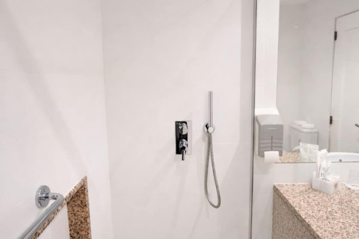 A modern bathroom with a glass shower enclosure, a granite countertop, and a mirror reflecting the room.