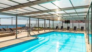A covered swimming pool with lounge chairs and a digital temperature display. - Hotel Boa-Vista (Porto)