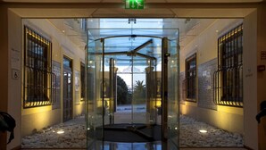 A revolving door with glass panels and metal bars, leading to a lobby area with a tiled floor and a red carpet. - Hotel Boa-Vista (Porto)