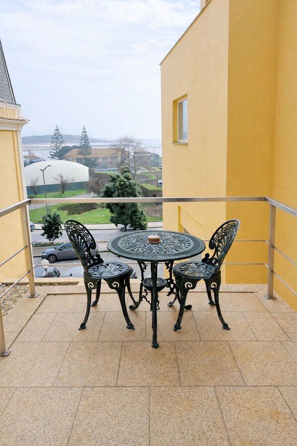 Un balcón con una mesa redonda y cuatro sillas, con vista a un paisaje urbano con edificios y árboles.