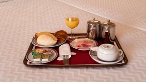 A hotel room with a neatly made bed, a bedside table with a lamp, and a tray with breakfast items including eggs, toast, and juice. -  Stay Hotel Porto Centro Antas (Porto)