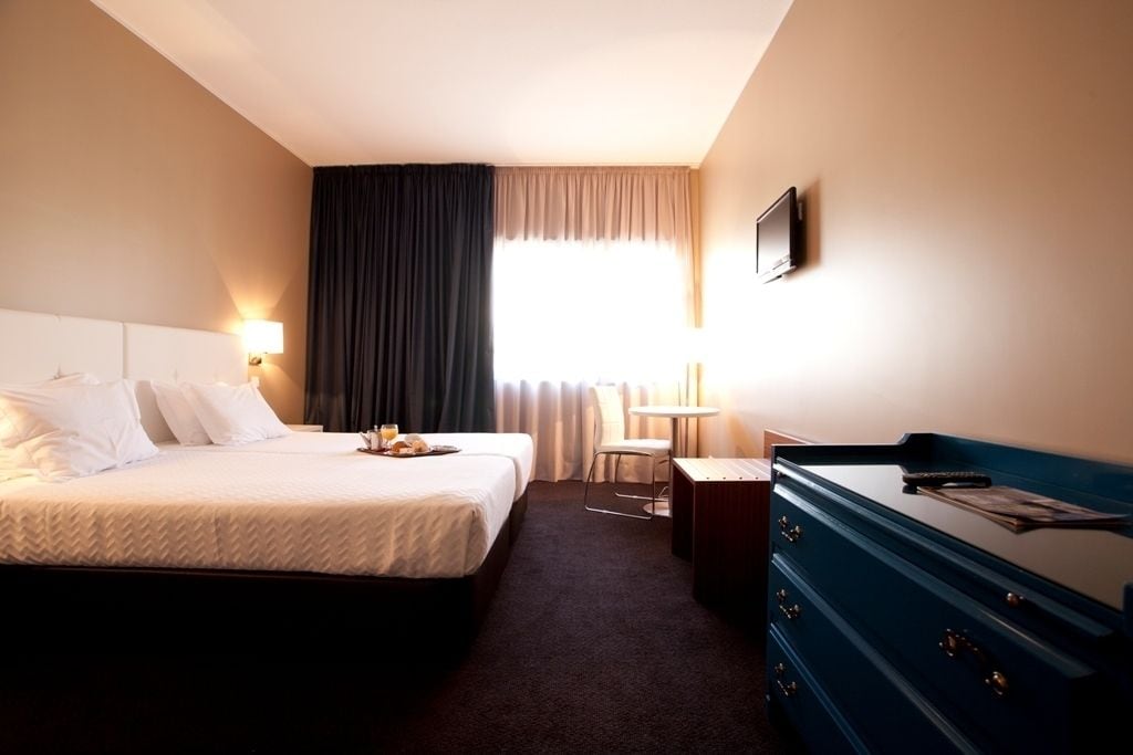 A hotel room with a large bed, a desk, a chair, a dresser, and a TV on the wall.