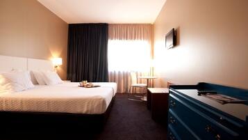 A hotel room with a large bed, a desk, a chair, a dresser, and a TV on the wall.