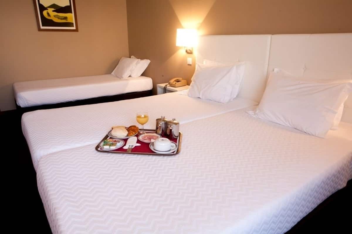 Una habitación de hotel con dos camas, una bandeja de desayuno y una mesita de noche con lámpara.