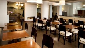 A modern dining area with wooden tables and chairs, large pendant lights, and a visible kitchen area in the background. -  Stay Hotel Porto Centro Antas (Porto)