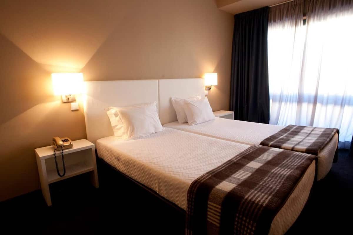 Habitación de hotel con dos camas, teléfono junto a la cama y ventana con cortinas.