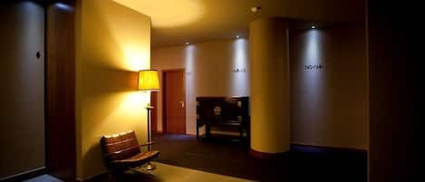 Un pasillo de hotel con un banco, una lámpara y una recepción.