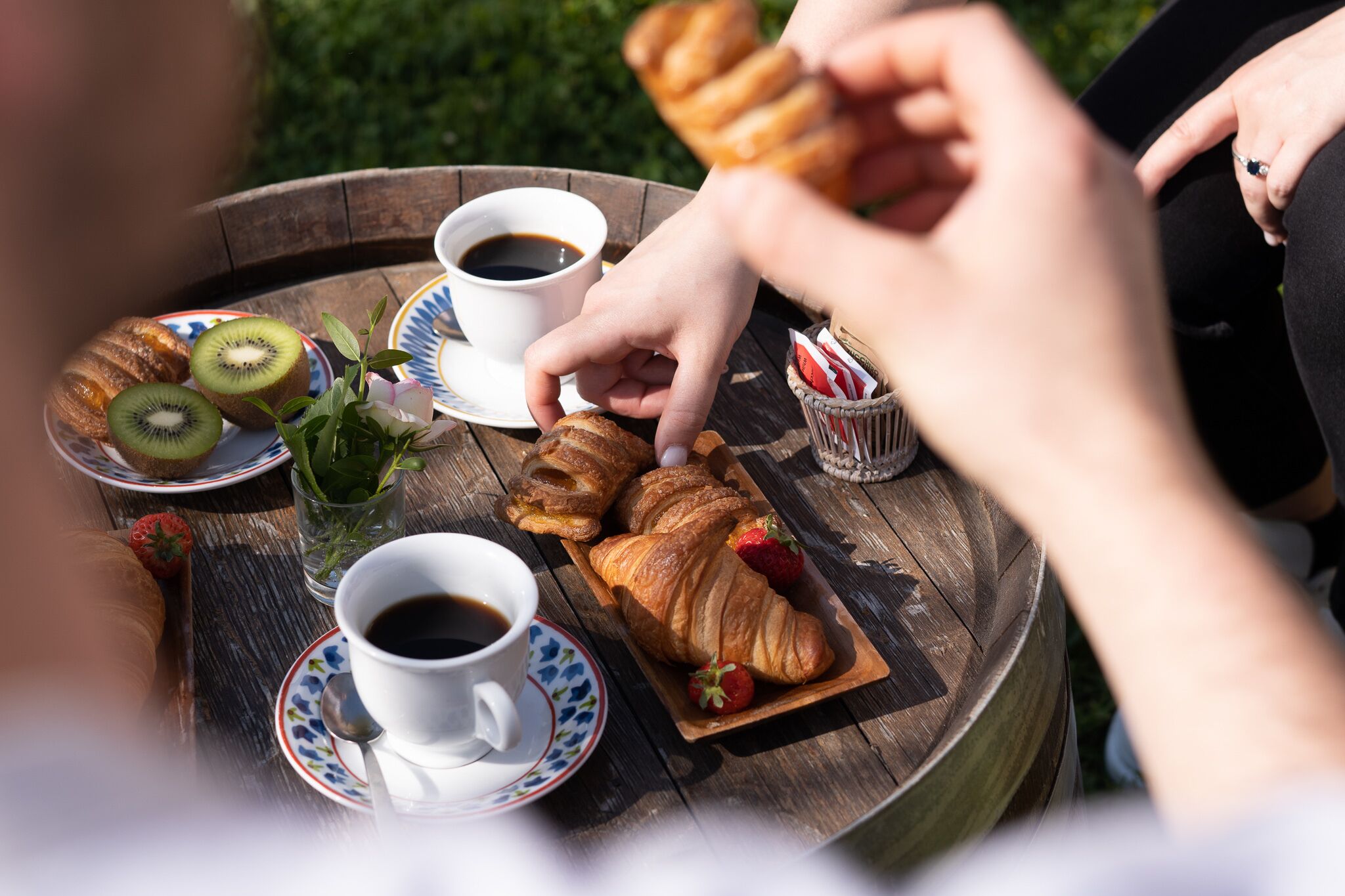 A round wooden table with a plate of croissants, a cup of coffee, a glass of water, and a slice of kiwi.