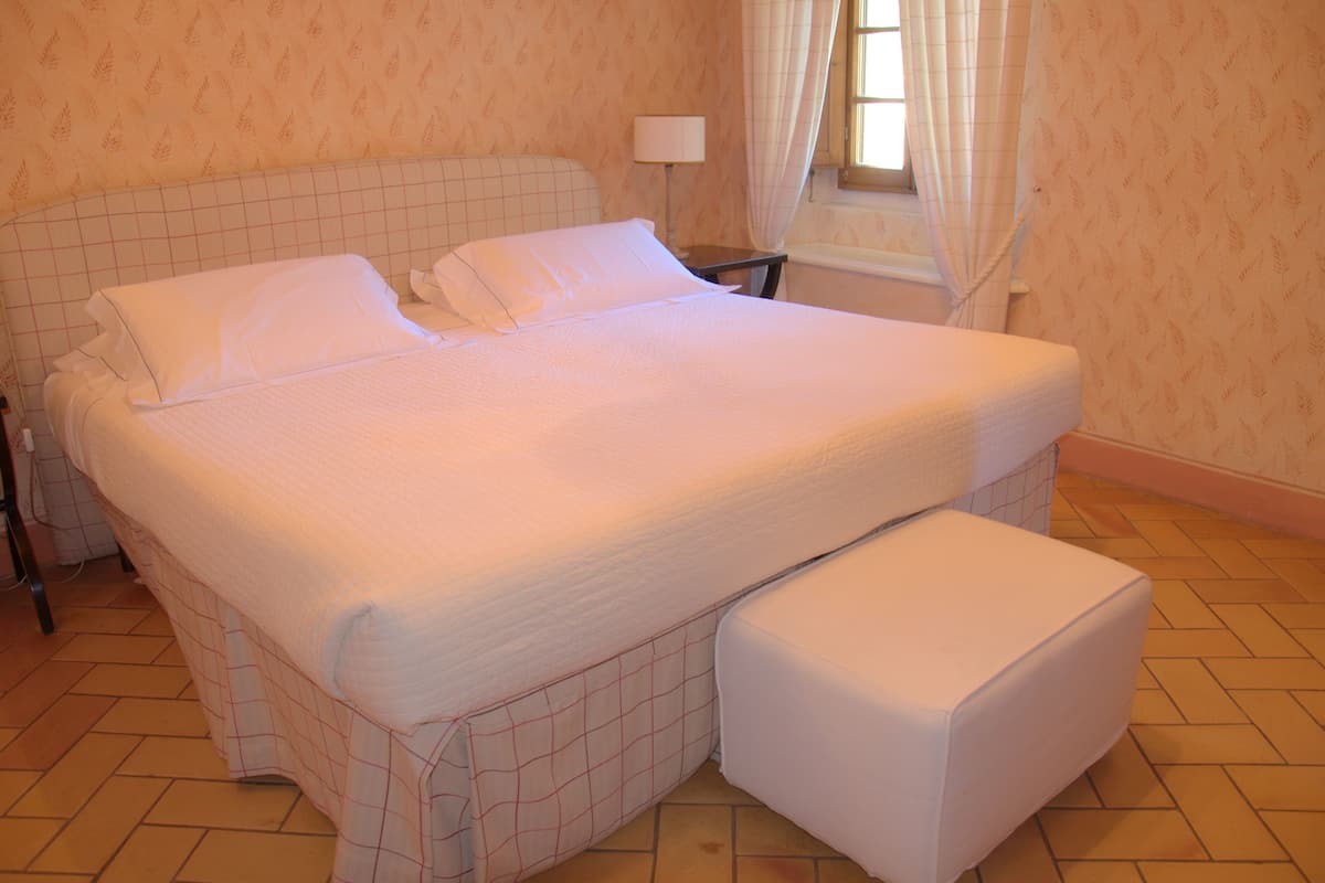 Un lit bien fait, avec une tête de lit, une table de chevet et une fenêtre avec des rideaux.