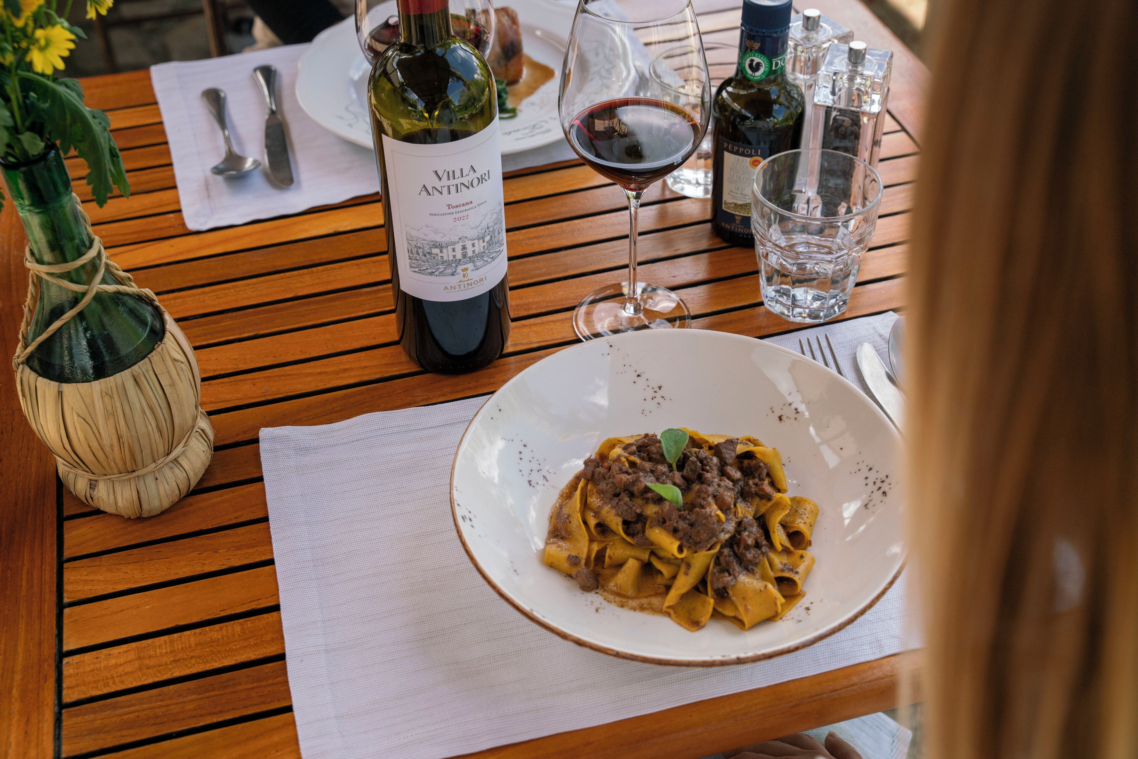 A wooden table with a plate of pasta, a wine bottle, and glasses.