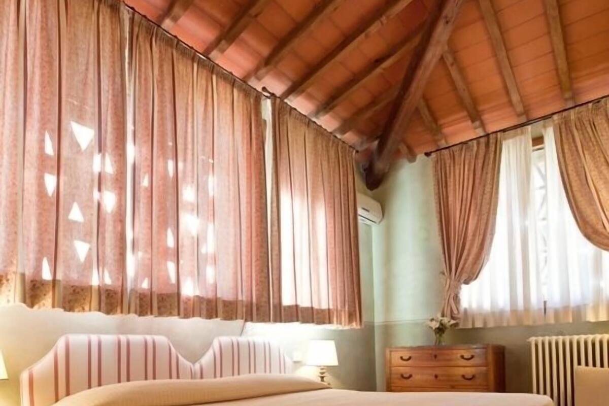 Une chambre à coucher avec un grand lit, une tête de lit en bois, des rideaux, une commode et un radiateur.