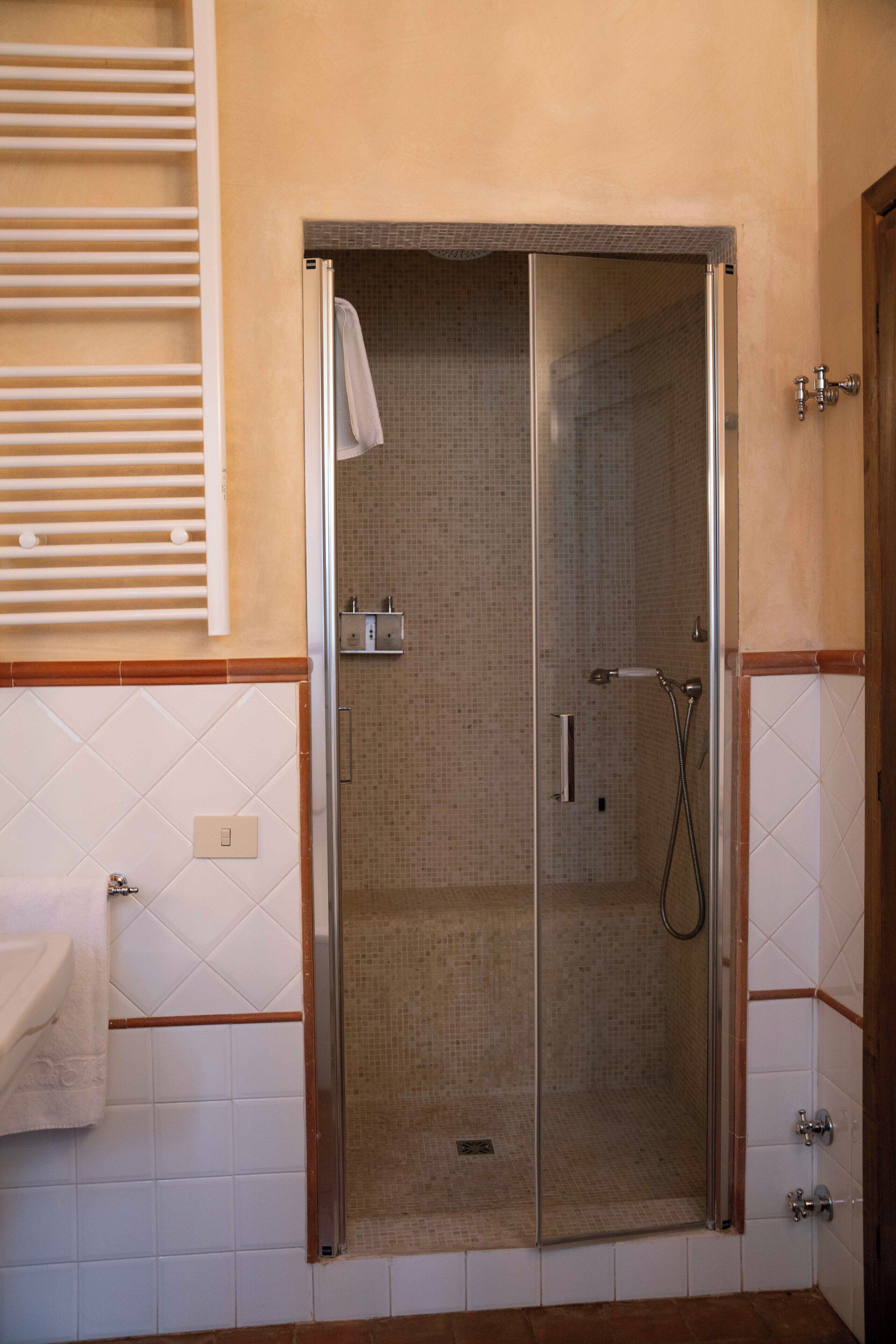 Una ducha a nivel con mampara de vidrio, paredes de azulejos y una toalla colgada en la puerta.