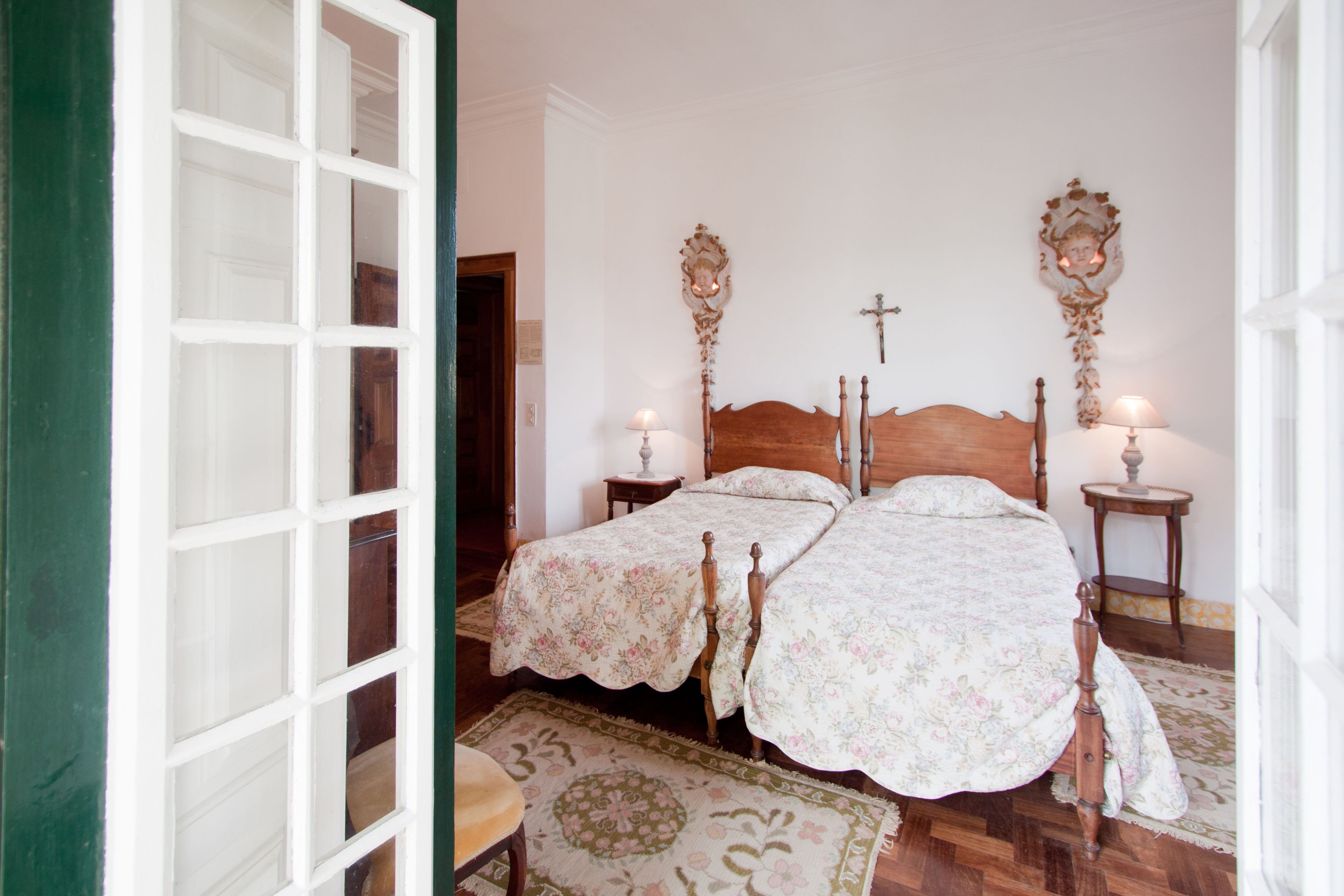 A room with two wooden beds, a wooden headboard, a small bedside table with a lamp, and a patterned rug.