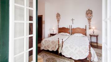 A room with two wooden beds, a wooden headboard, a small bedside table with a lamp, and a patterned rug.