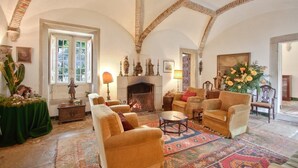 A spacious living room with high ceilings, a fireplace, comfortable seating, and a large window providing natural light.