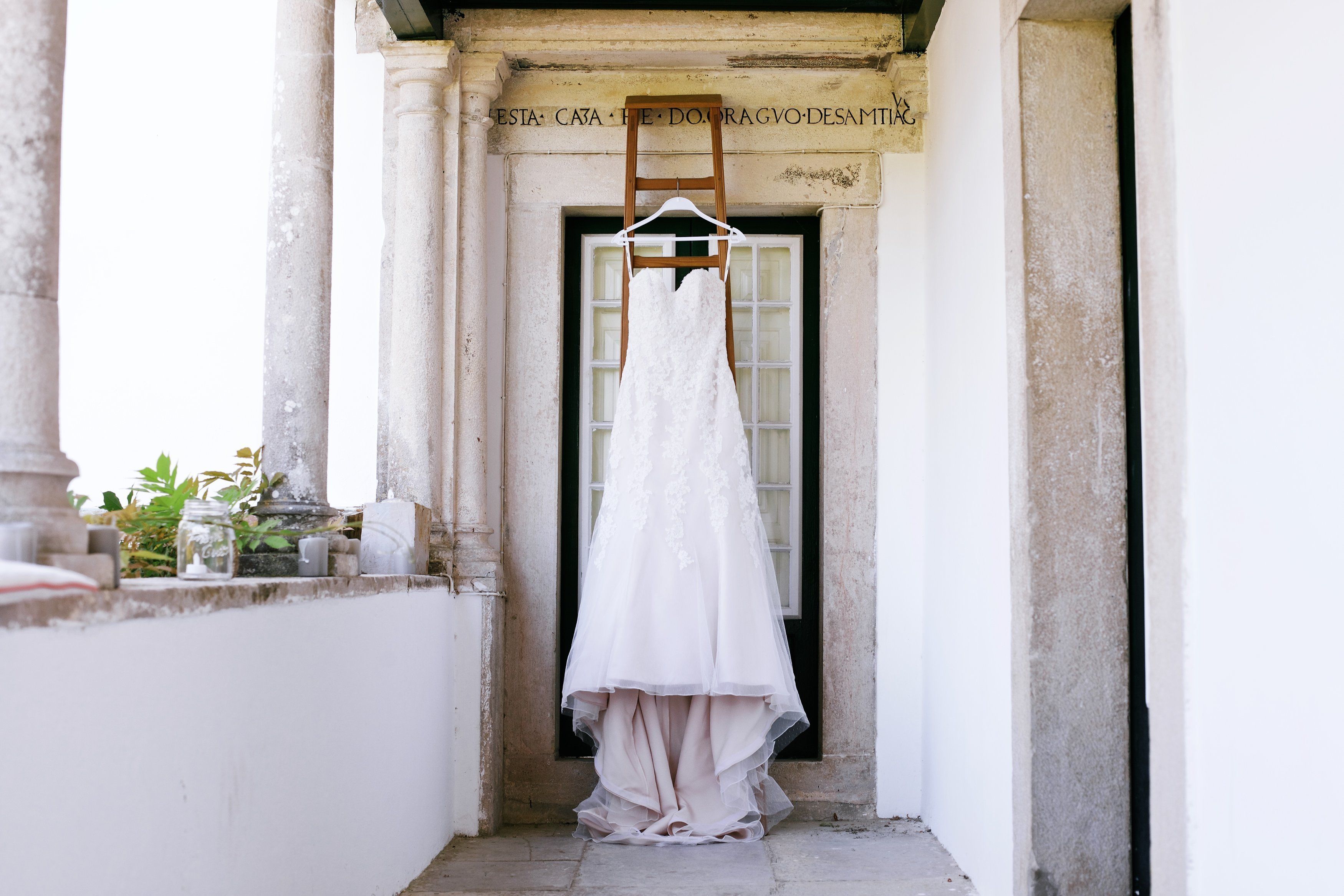 Un vestido de novia blanco colgado de un perchero de madera en un estrecho vano con columnas.