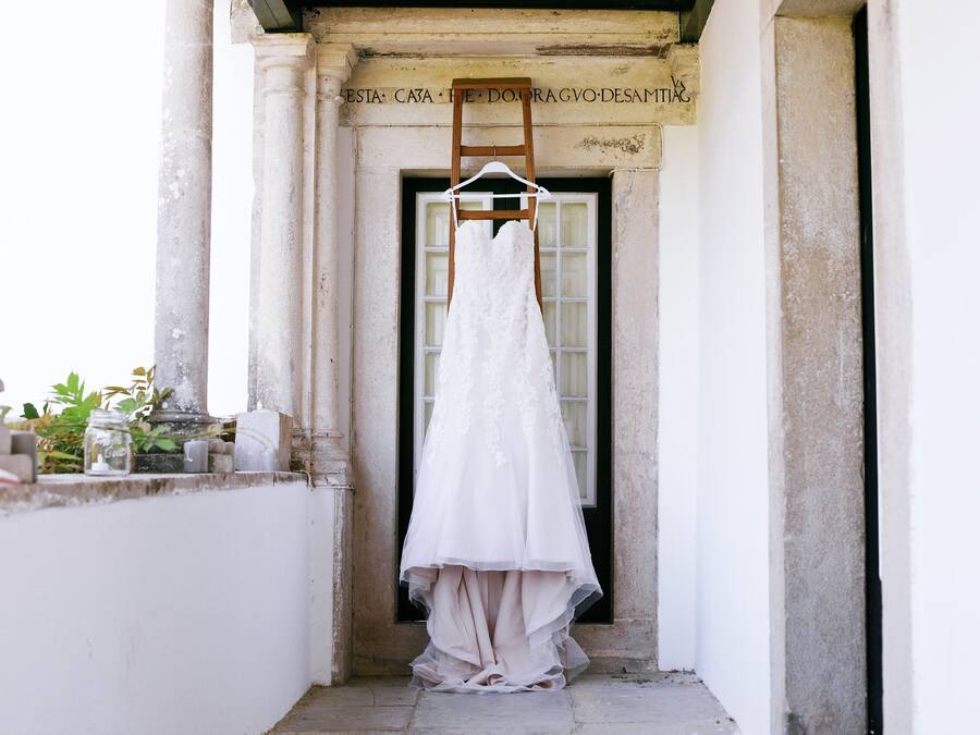 Un vestido de novia blanco colgado de un perchero de madera en un estrecho vano con columnas.