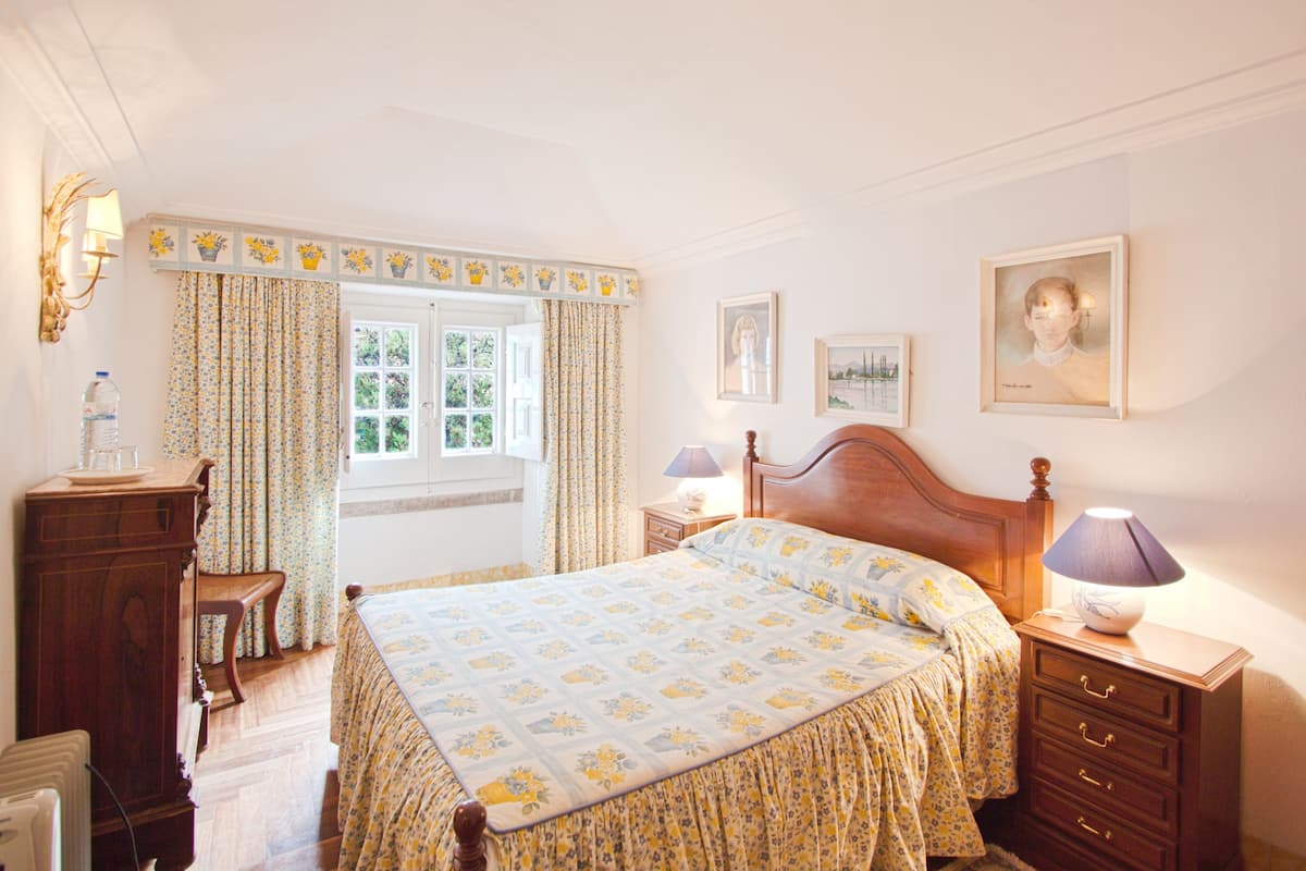Een slaapkamer met een houten bed, een nachtkastje met een lamp, een dressoir en een raam met gordijnen.