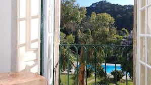 A balcony with a view of a pool and greenery, a marble table, and a door leading outside.