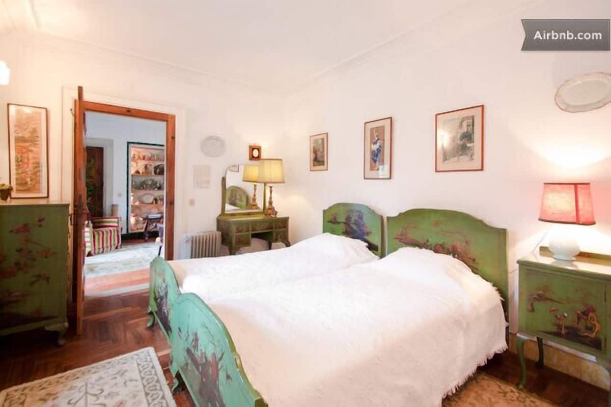Een slaapkamer met een tweepersoonsbed, een dressoir, een nachtkastje, een lamp en een deur naar een andere kamer.