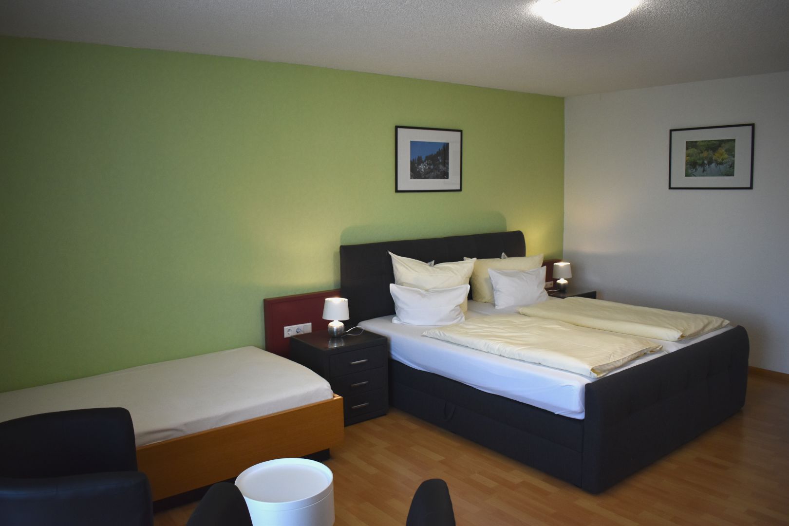 A hotel room with a single bed, a smaller bed, a desk, and a chair. There are two bedside tables with lamps.