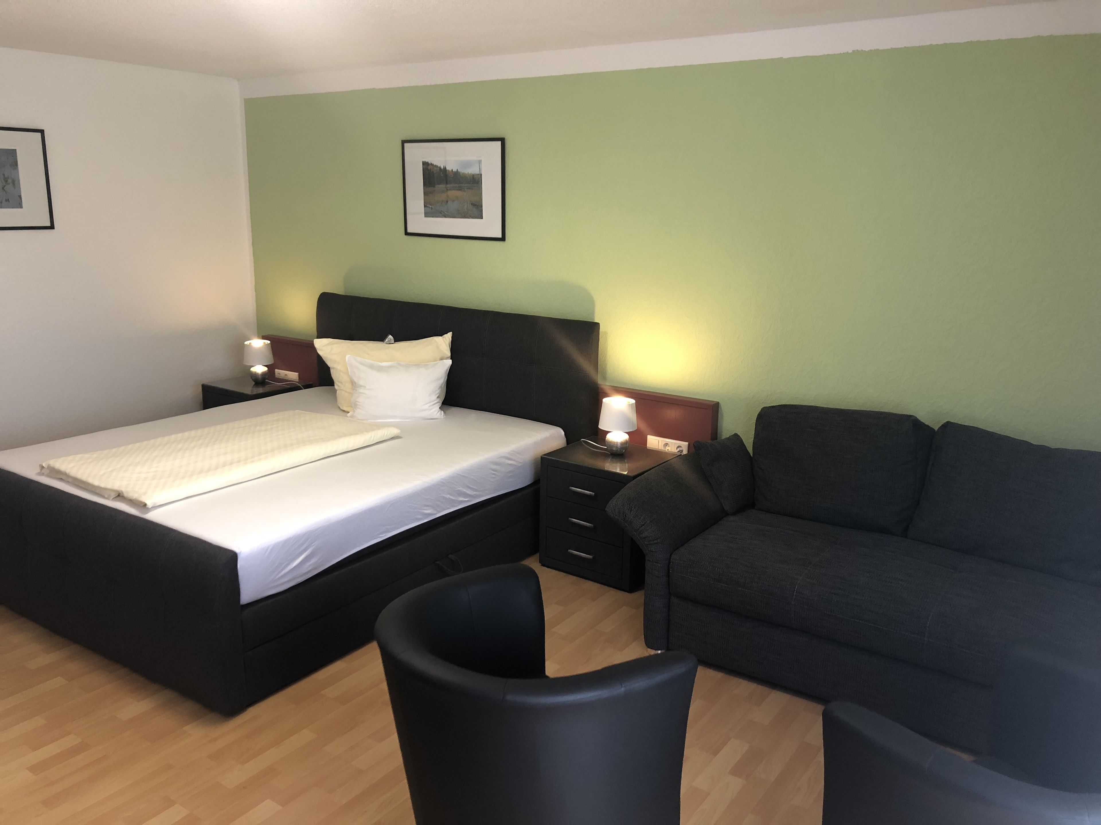 Un dormitorio con cama, mesitas de noche, una lámpara, un sofá y un cuadro en la pared.