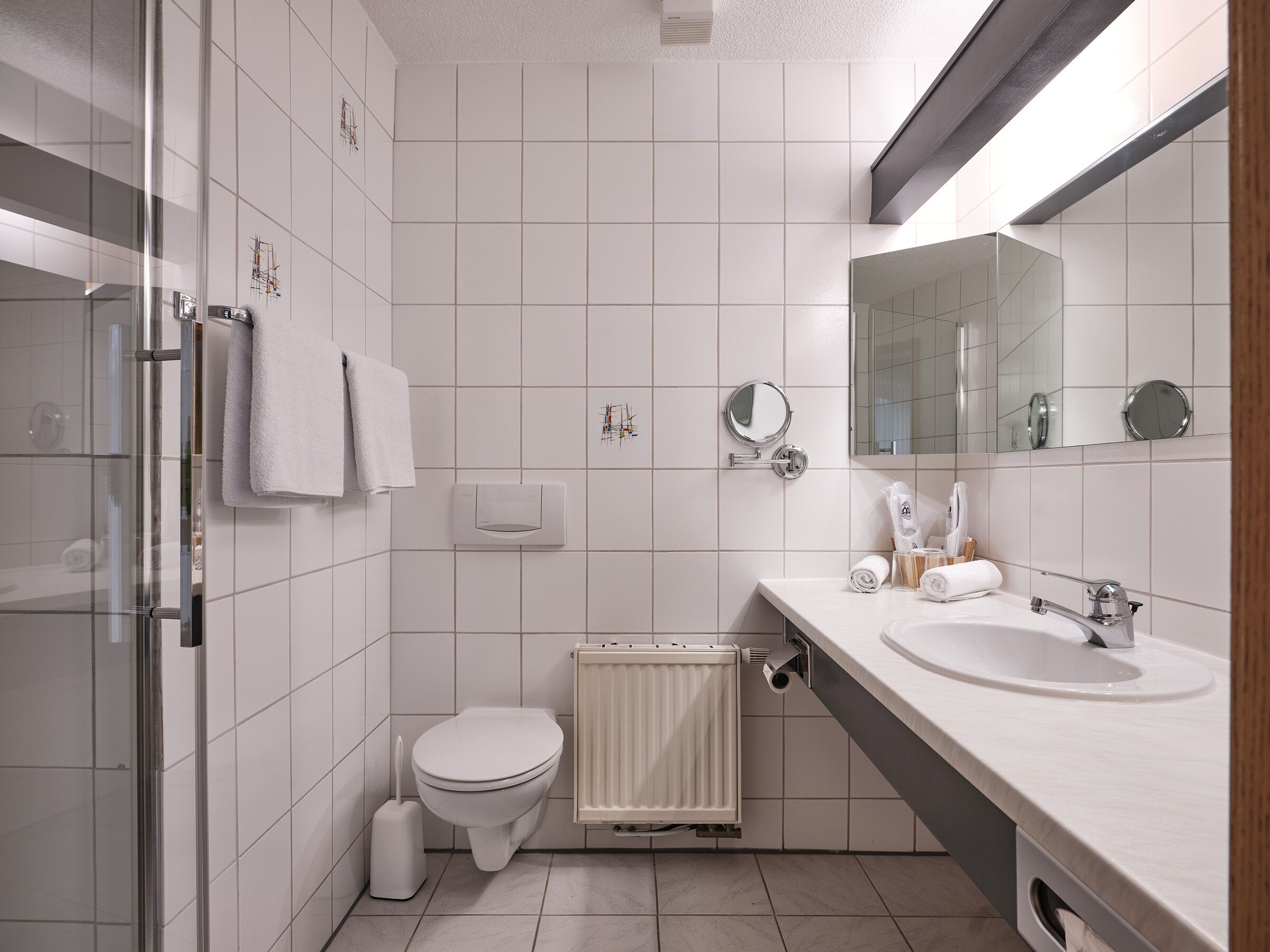 Un bagno moderno con box doccia in vetro, un water, un lavandino e uno specchio.
